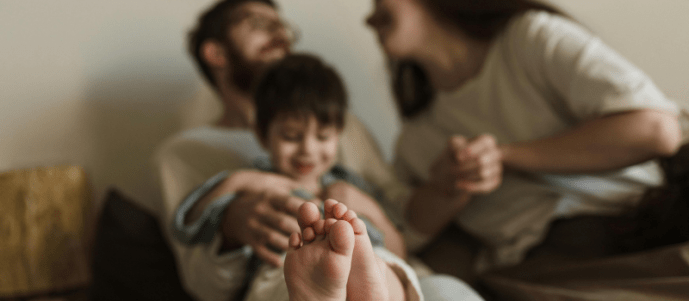 parents sit closely with a smiling young child on a couch, showing warmth and supervision, highlighting adults’ role in child safety through attentive care, emotional support, and a secure family environment.