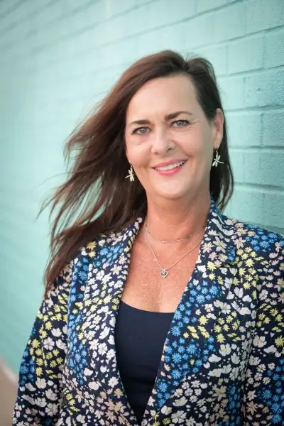 Beth Jones, Leadership Performance Strategist, in front on turquoise painted brick wall
